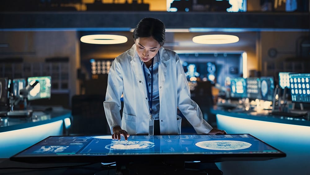 Junge Frau in Laborsituation arbeitet konzentriert an einem großen Touch-Screen-Tisch.