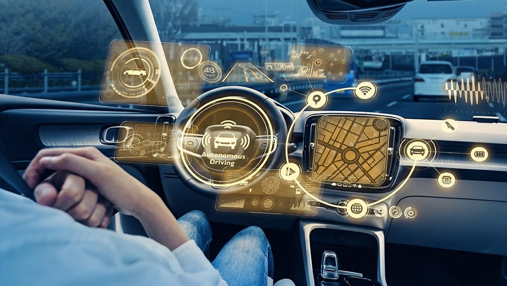 Innenansicht eines Autocockpits mit Fahrer, der die Hände weg vom Lenkrad hat. Vor Lenkrad und andern Bedienelementen erleuchet ein virtuelles Dashboard, welches Mobilität der Zukunft symbolisiert.